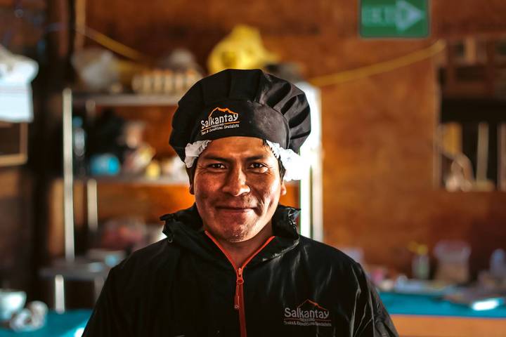 A smiling man wearing a chef's hat in a cozy indoor setting.