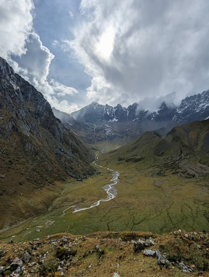 A broad valley nestled between mountain ranges under a dramatic cloudy sky.
