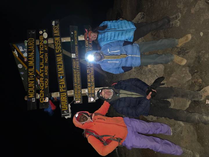Group of climbers at the Uhuru Peak sign on Mount Kilimanjaro at night.