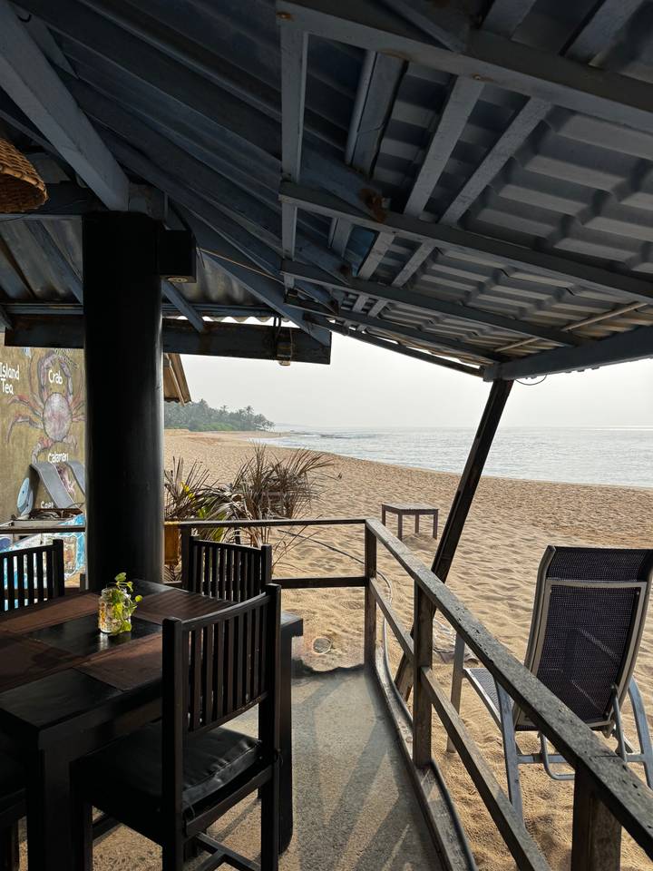 Vue sur la plage depuis sous un toit avec une mer calme et un rivage sablonneux.