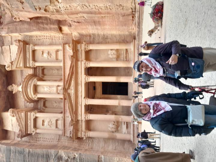 Two people in scarves and jackets posing in front of ancient Petra's Treasury.