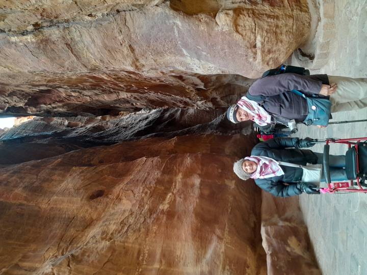 Two people wearing scarves amid the narrow canyon walls of the Siq in Petra.
