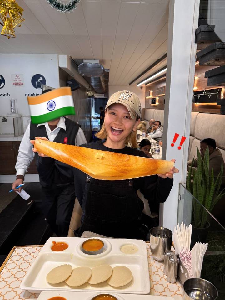 Person in a restaurant holding a large dosa with excitement.