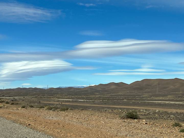 Flat landscape with distant hills and power lines under a blue sky with unique cloud formations.