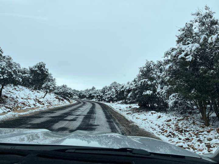 Snow-covered road through mountainous forest landscape.