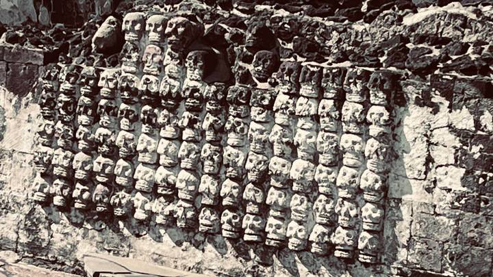 Rotswand met rijen van uitgehouwen schedels op een archeologische vindplaats.