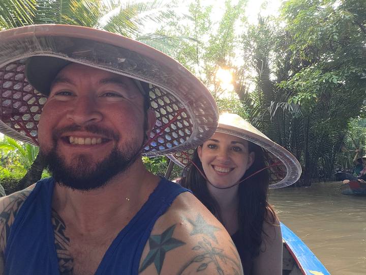 Pareja sonriendo mientras usan sombreros cónicos en un paseo en bote