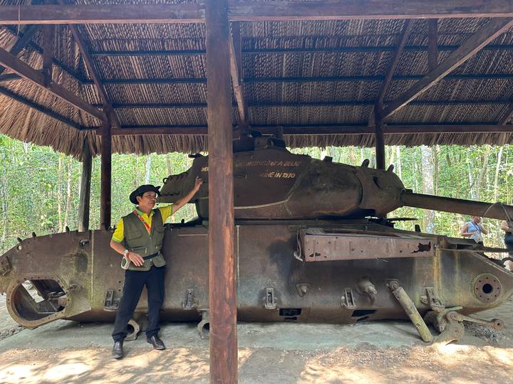 Guía mostrando un tanque antiguo bajo un refugio de paja