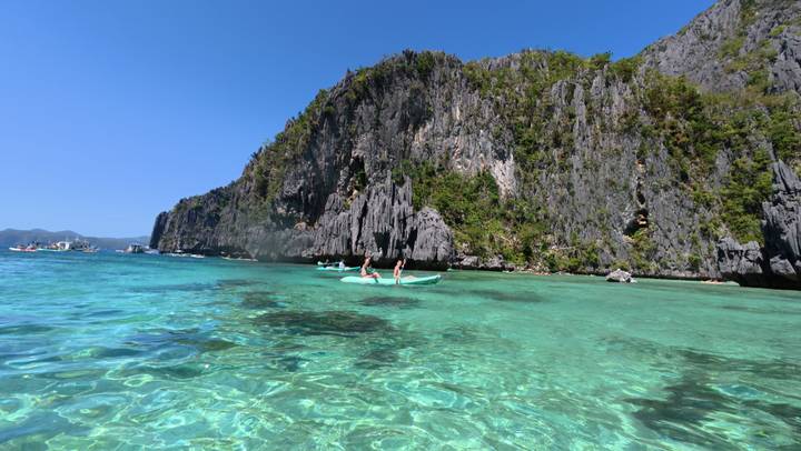 Kayakers exploring rock formations on clear water.