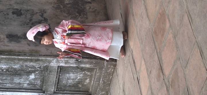 Kind gekleed in traditionele kleding, staand in een rustieke omgeving.