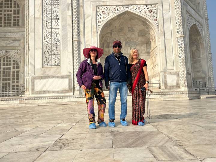 Three tourists wearing protective shoe covers near the Taj Mahal.