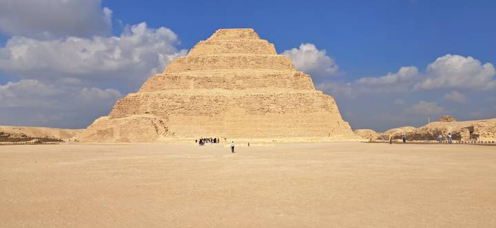 Step pyramid in the desert with tourists exploring around.