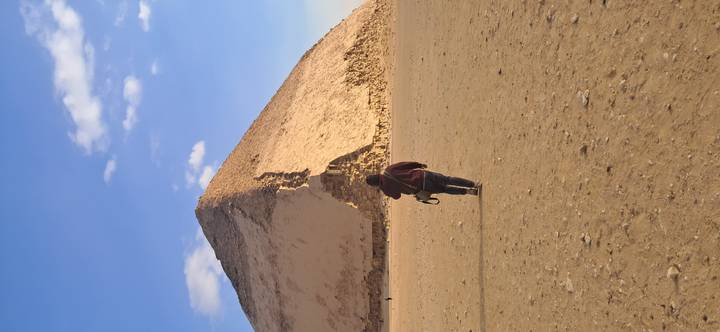 Individual walking towards a desert pyramid under a clear sky.