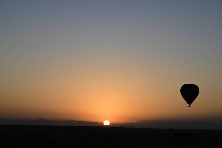 Silhouette of a hot air balloon against a sunrise in the savannah.