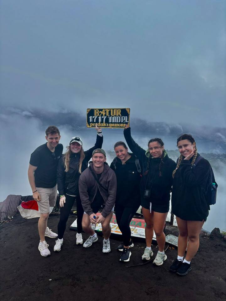 Group of friends holding a sign at a summit with foggy background.