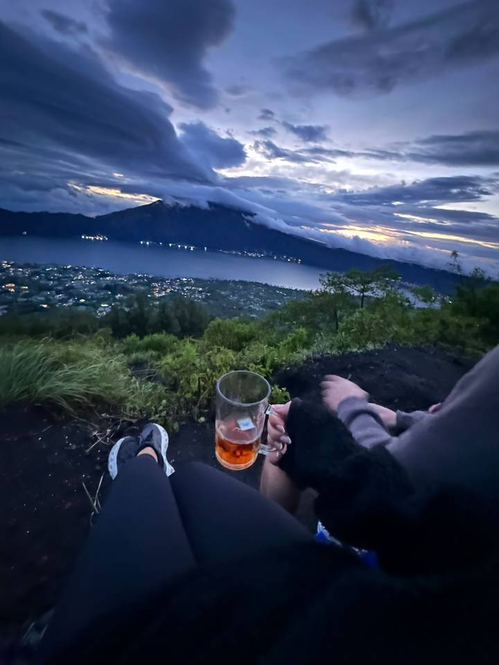 View from a mountain with a lake, focusing on someone holding a drink.