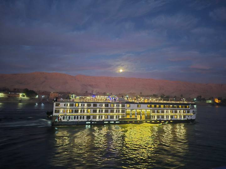Illuminated cruise ship sailing on a river at dusk.