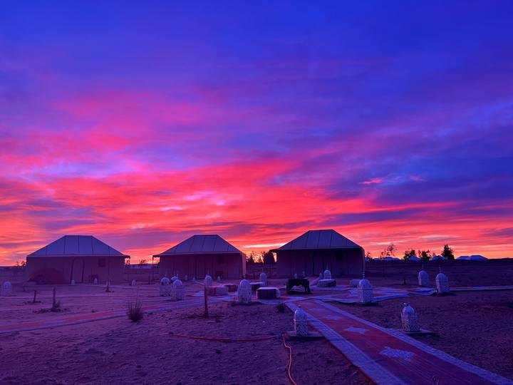 Colorful sunset sky over desert huts, creating a vibrant landscape with scattered tents.