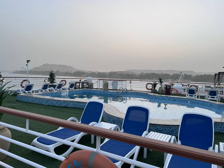 Cruise ship deck with a pool overlooking the river and distant hills.