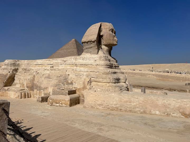 Sphinx with pyramid in the background under a clear blue sky.