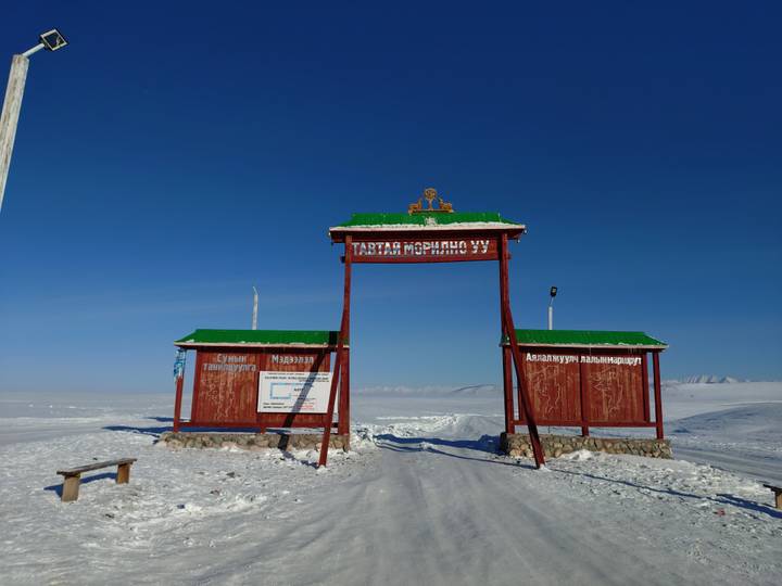 Entrance sign to a snowy landscape with a clear blue sky.