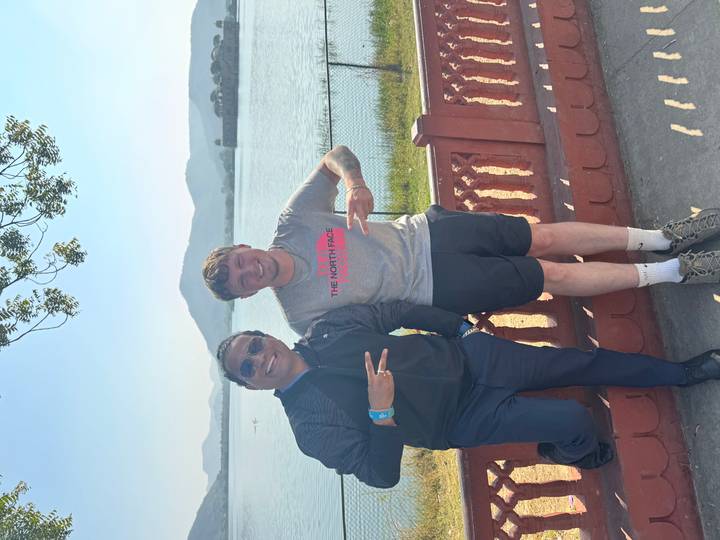Two men posing by a lakeside with mountains in the background.