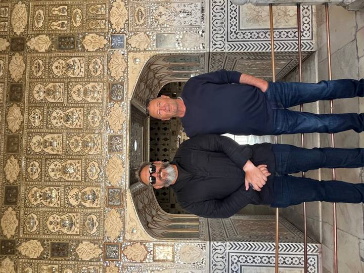 Two men stand before intricate mirrored mosaic walls inside Amber Fort's Sheesh Mahal.