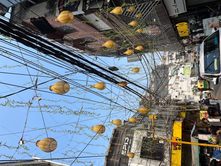 Urban street with a canopy of decorative gourds and tangled overhead wiring against blue sky.