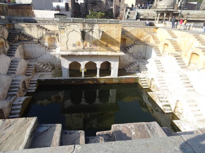 Symmetrical ancient stepwell with geometric stair patterns descending to green water.