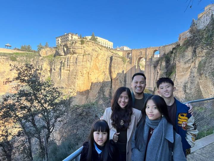 Smiling family with the dramatic Puente Nuevo bridge and cliffs of Ronda towering behind.