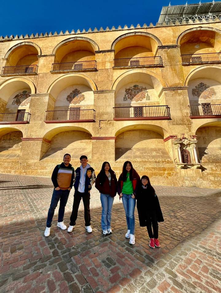 Family standing before sun-bathed arches and walls of a historic Andalusian building in Córdoba.