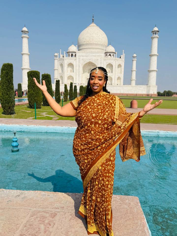 Woman in traditional sari posing joyfully before the reflecting pool with the Taj Mahal in the background.