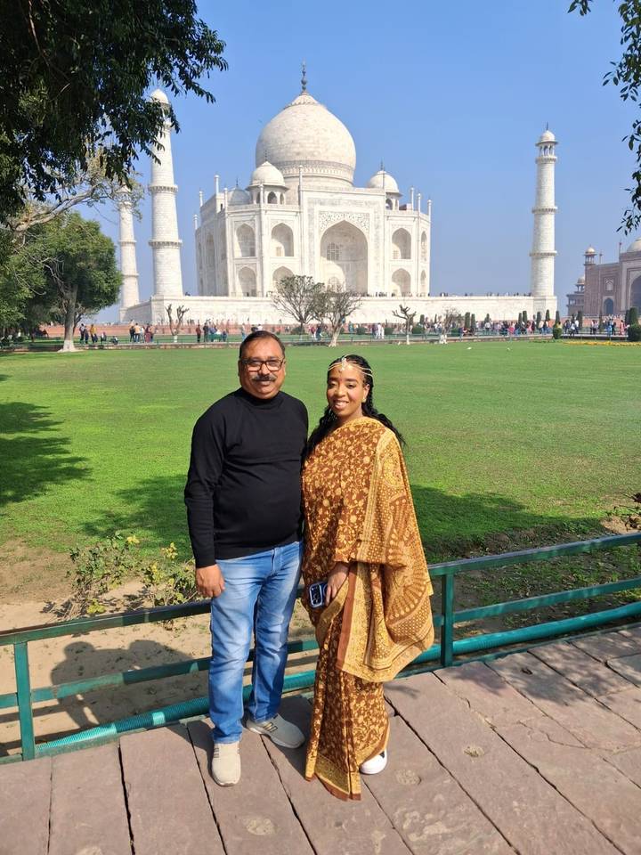 Tourist and guide posing with expansive green gardens and the Taj Mahal in the distance.