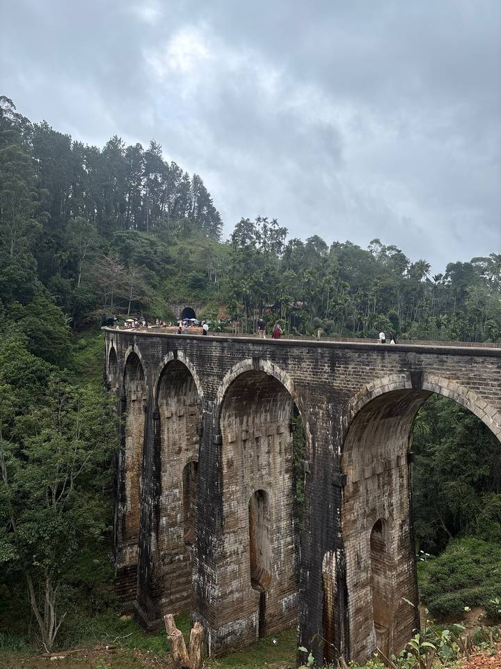 Travelers walk across the iconic Nine-Arches stone railway bridge spanning a lush jungle valley.