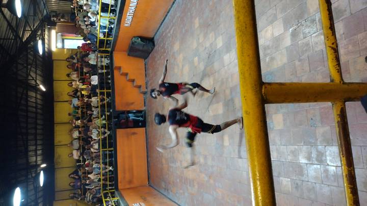 Traditional Kalaripayattu martial artists spar inside an arena with seated audience.