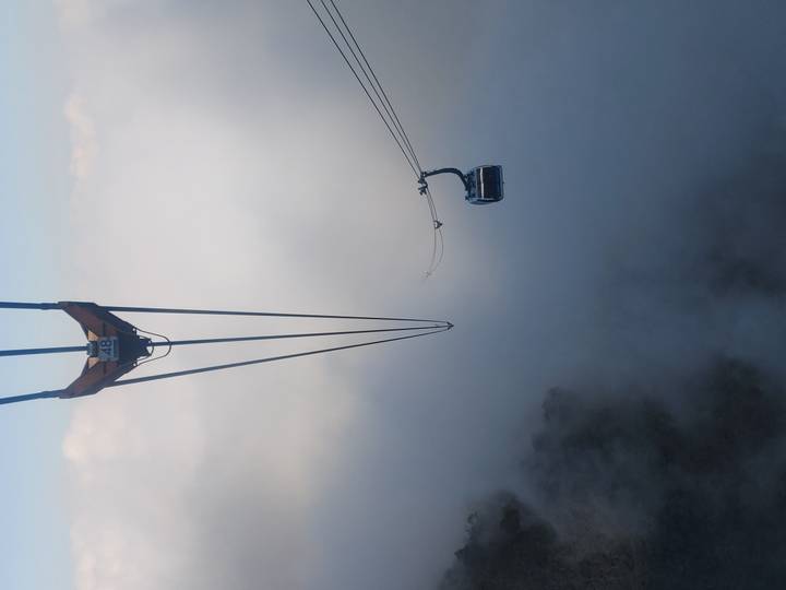 Cable car gliding through thick clouds high above forested mountains.