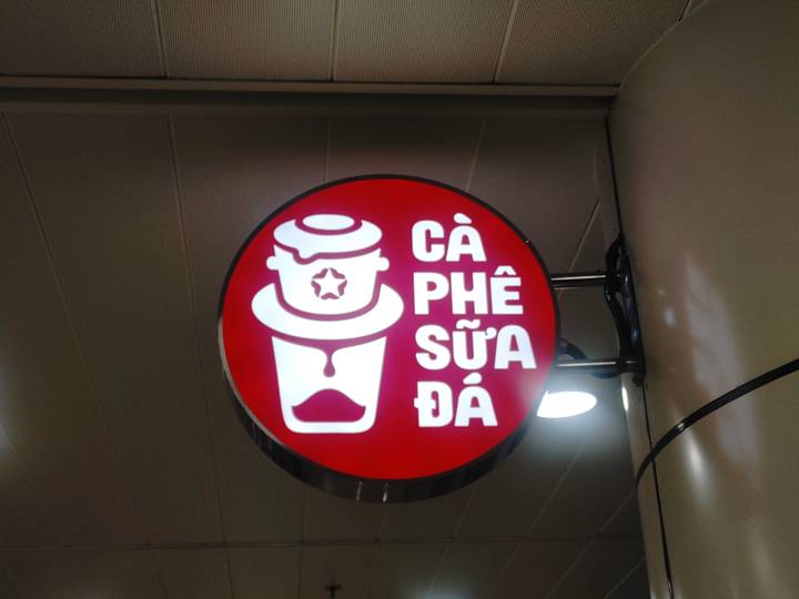 Round red illuminated sign reading 'Cà Phê Sữa Đá' depicting a Vietnamese coffee filter.