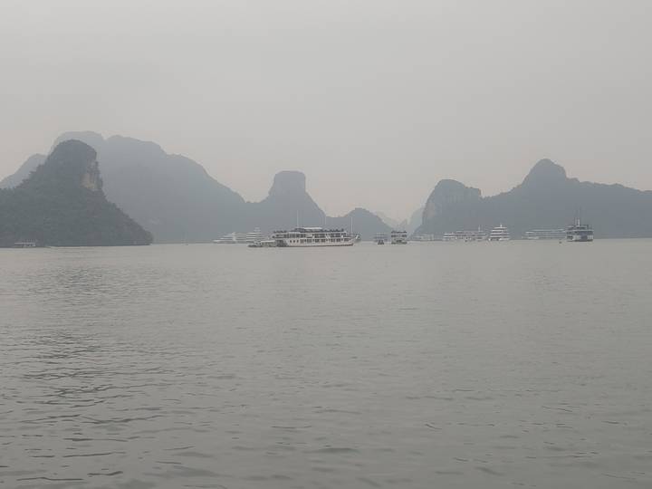 Grey hazy day on Halong Bay with karst islands and numerous cruise boats on calm water.