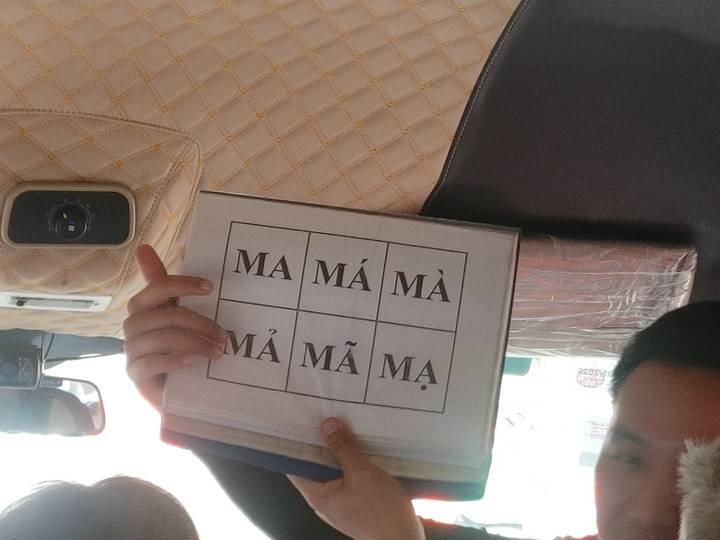 Tour guide holding a flash card inside minibus showing different Vietnamese tonal marks.