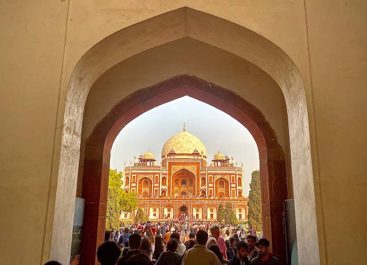 Crowds gather in front of Humayun's Tomb, framed perfectly by a sandstone archway entrance.