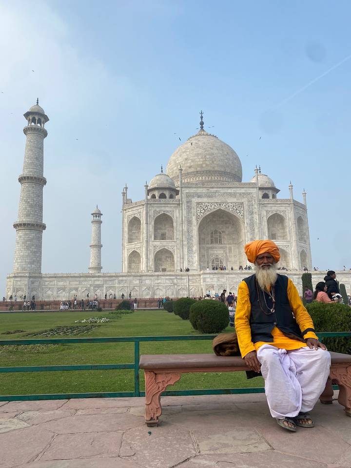 An elderly man in an orange turban stands proudly before the Taj Mahal's marble backdrop.