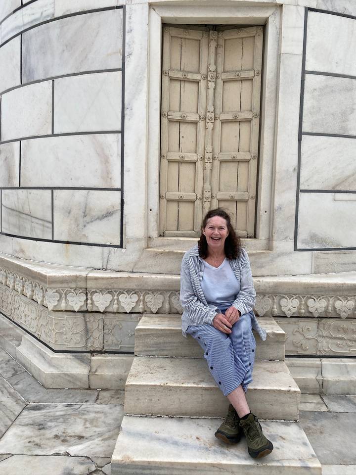 A smiling woman sits on a marble bench beside ornate stonework inside the Taj Mahal complex.