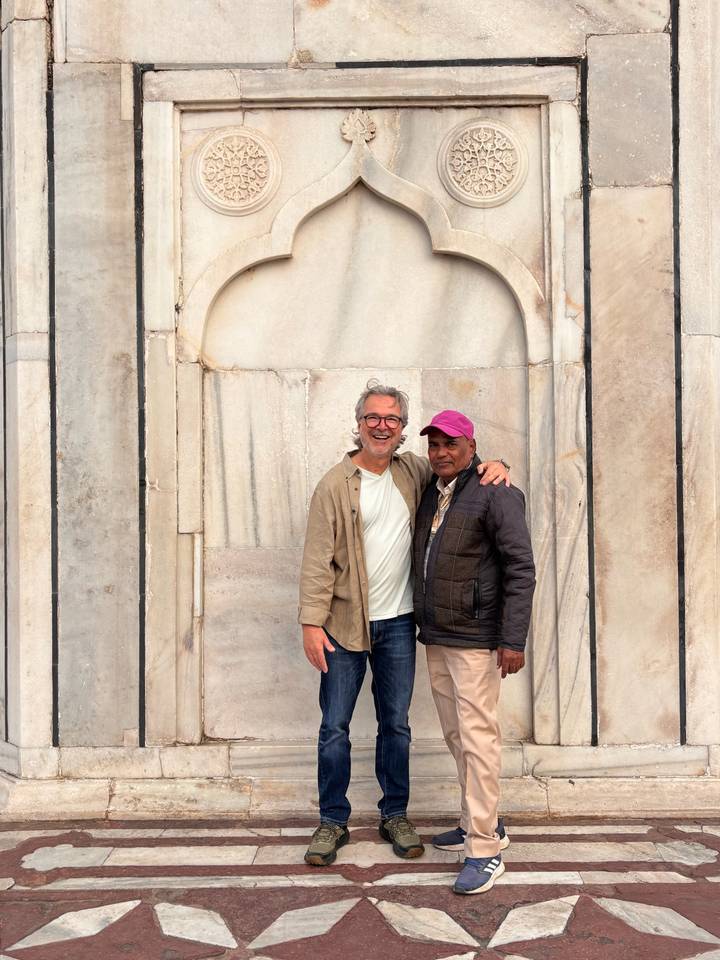 Two men stand arm-in-arm smiling against a marble niche of the Taj Mahal.