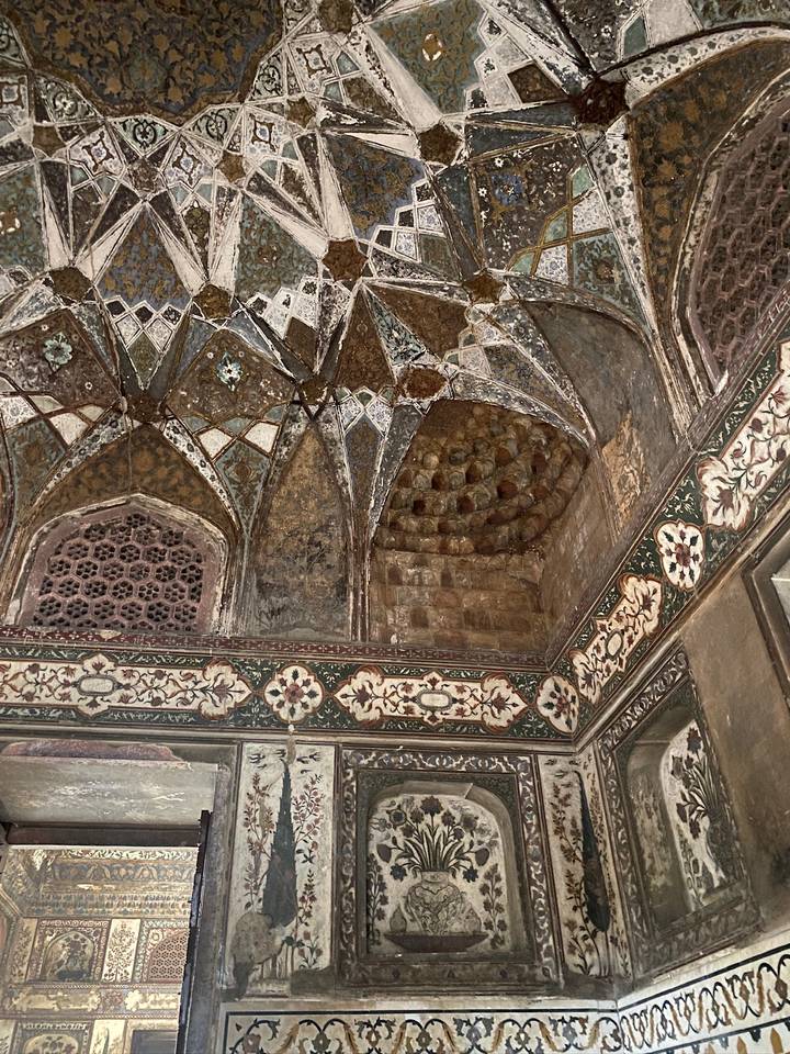 Detailed Mughal frescoes and geometric patterns decorate the vaulted ceiling of an historic monument.