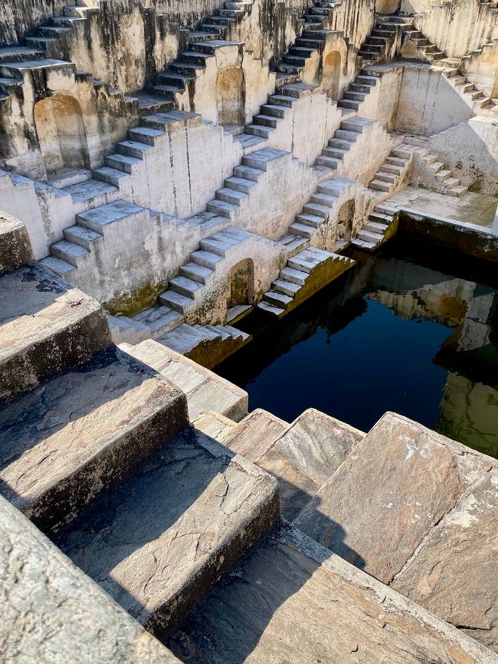 Stone steps descend into a rectangular water tank, their reflections mirrored on the dark surface.