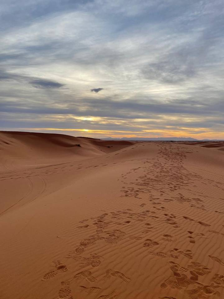 Serene sunset over smooth orange sand dunes with footprints leading into the distance.