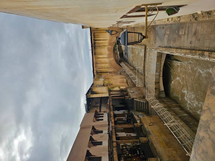 Fast-flowing muddy river through an old medina lined with weathered stone buildings and bridges.