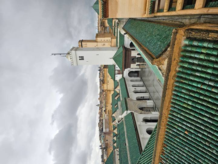 Rooftop view over the green-tiled courtyard and minaret of a historic Fes mosque.