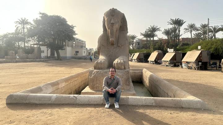 A traveller sits cross-legged before the alabaster Sphinx of Memphis on a hazy morning.