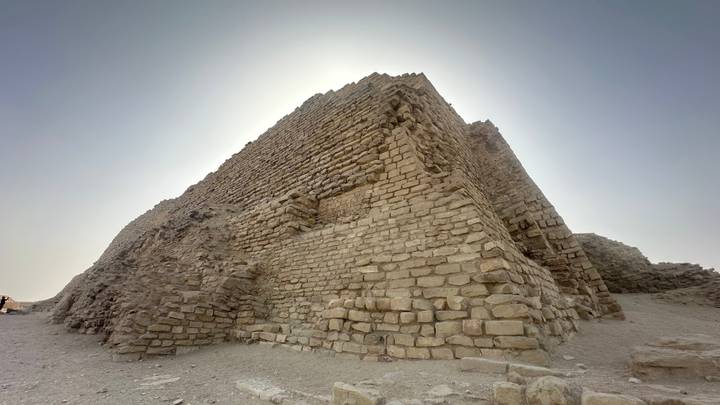 A dramatic low-angle view of ancient pyramid masonry blocks silhouetted against the bright desert sun.